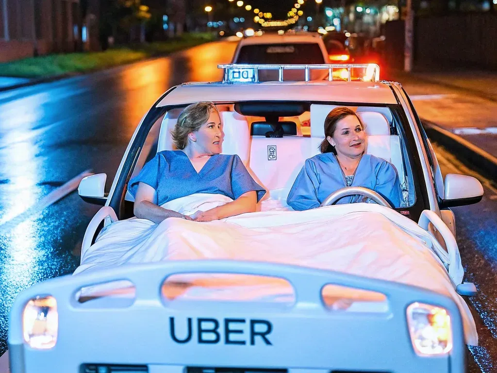 Two nurses dressed in scrubs, riding on a hospital bed modified as an Uber vehicle on a city street at night