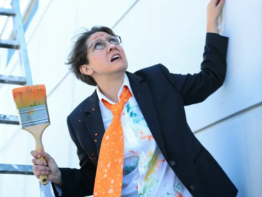 Professional painter climbing a ladder, paintbrush in hand, looking up while wearing a creatively splattered suit, reflecting the innovative spirit of online creative education