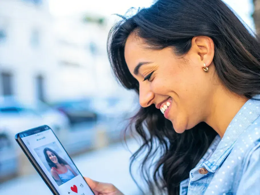 A woman smiling serenely while looking at her phone, showcasing a curated dating profile.