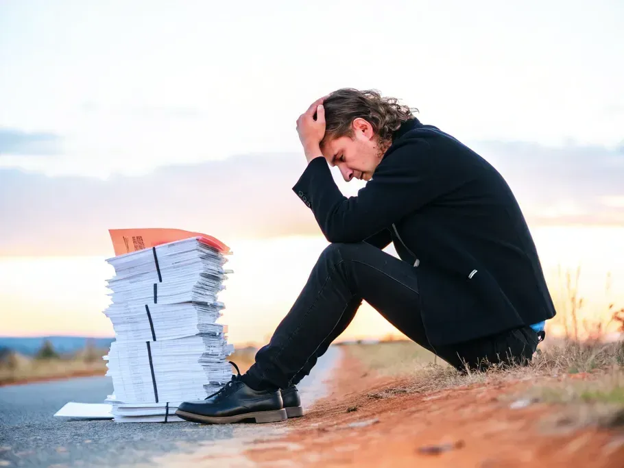 A young startup employee seated beside a stack of financial documents, expressing a mixture of burden and hope.