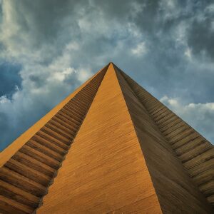 Upward view of a towering pyramid against a stormy sky, symbolizing strong market segment foundations.