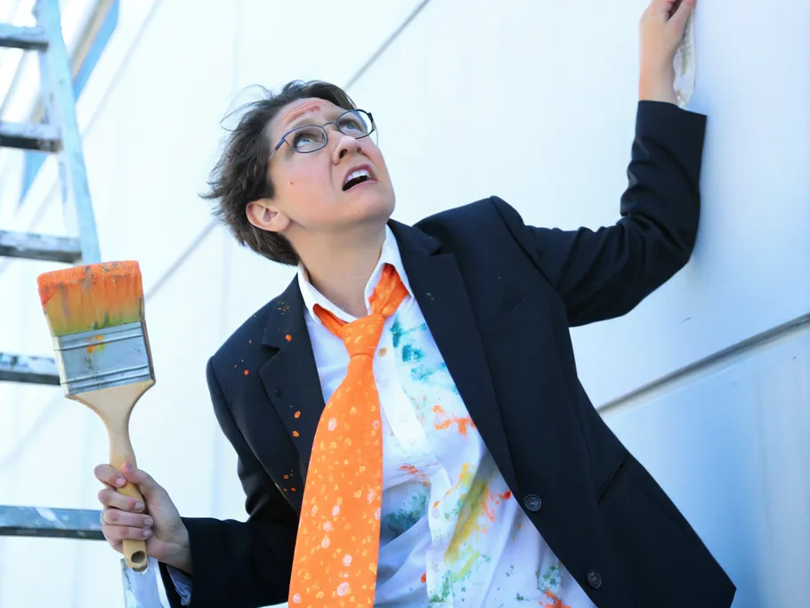 Professional painter climbing a ladder, paintbrush in hand, looking up while wearing a creatively splattered suit, reflecting the innovative spirit of online creative education