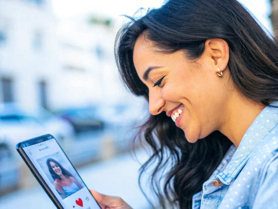 A woman smiling serenely while looking at her phone, showcasing a curated dating profile.