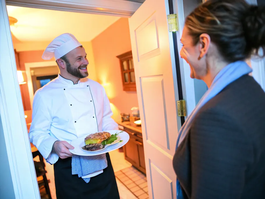A chef presenting a gourmet meal in a cozy home kitchen, bringing delight to a busy professional at their doorstep.