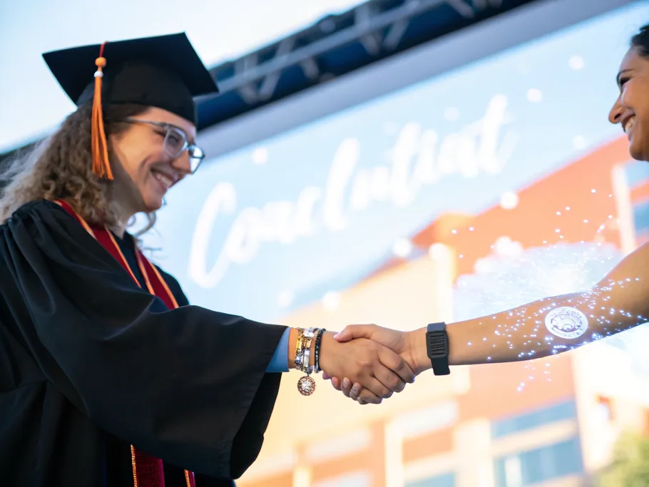 A close-up of two hands shaking, one with an academic ring and the other displaying a digital interface, symbolizing collaboration in mental health technology.