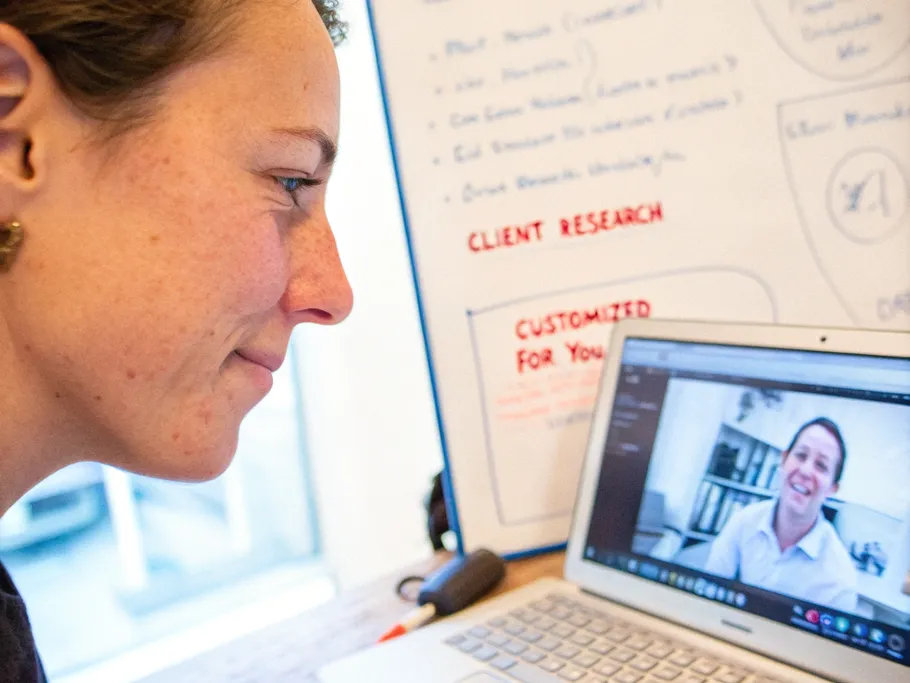Person recording a personalized video message on a laptop with a background of research notes and client information.